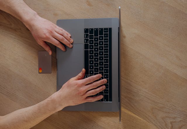 hand holding a credit card in front of a laptop